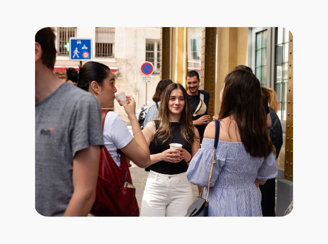 A lady smiling with a coffee cup in conversation with two other women facing the other way