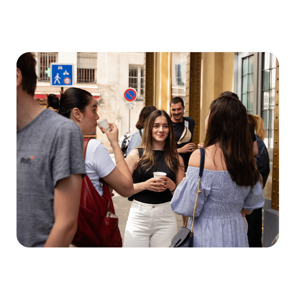A lady smiling with a coffee cup in conversation with two other women facing the other way