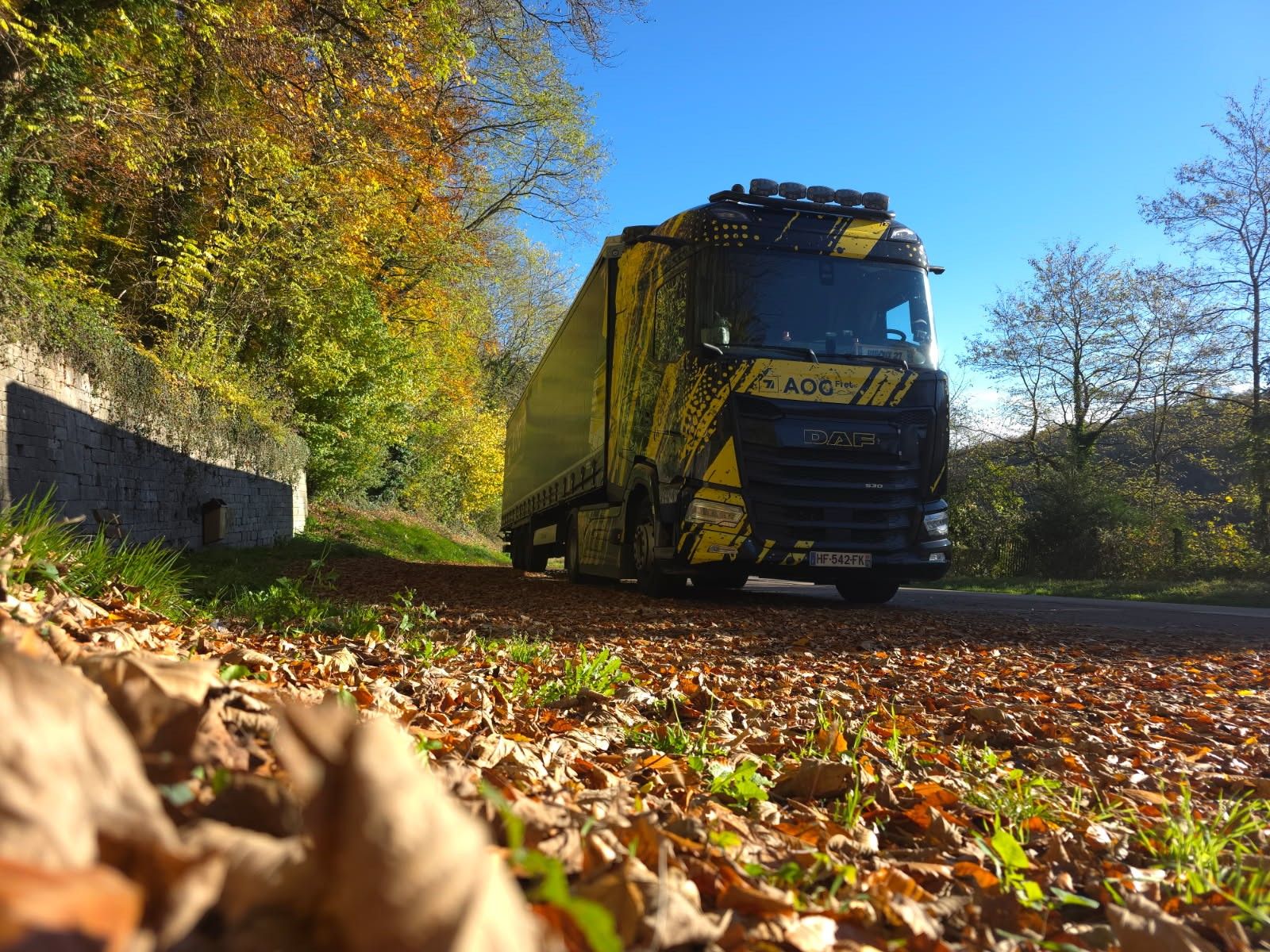 Camion d'AOG Fret du Groupe GSET circulant sur un chemin forestier couvert de feuilles d’automne.
