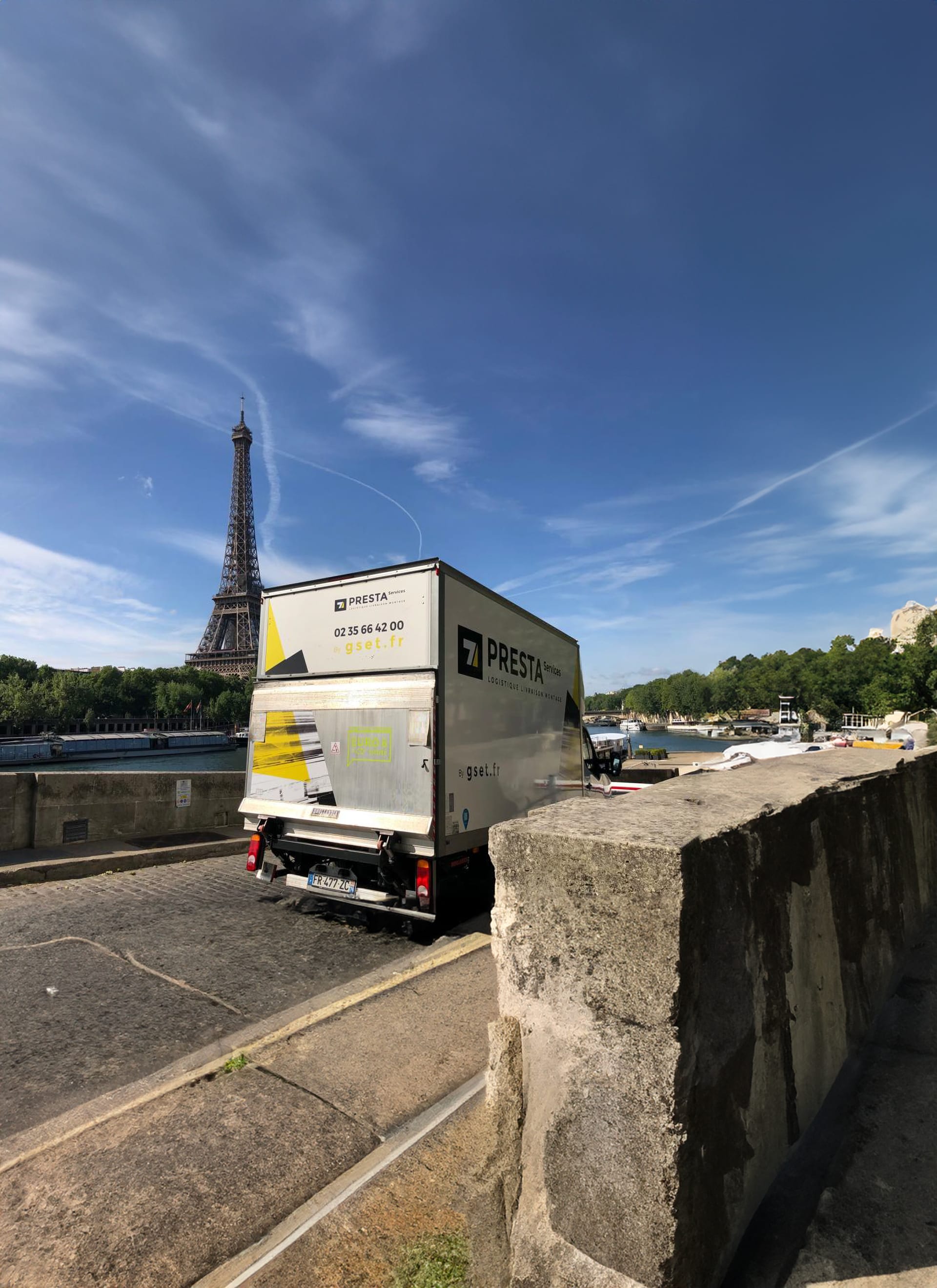 Camion de livraison PRESTA Services stationné près d’un pont, avec la tour Eiffel visible en arrière-plan.