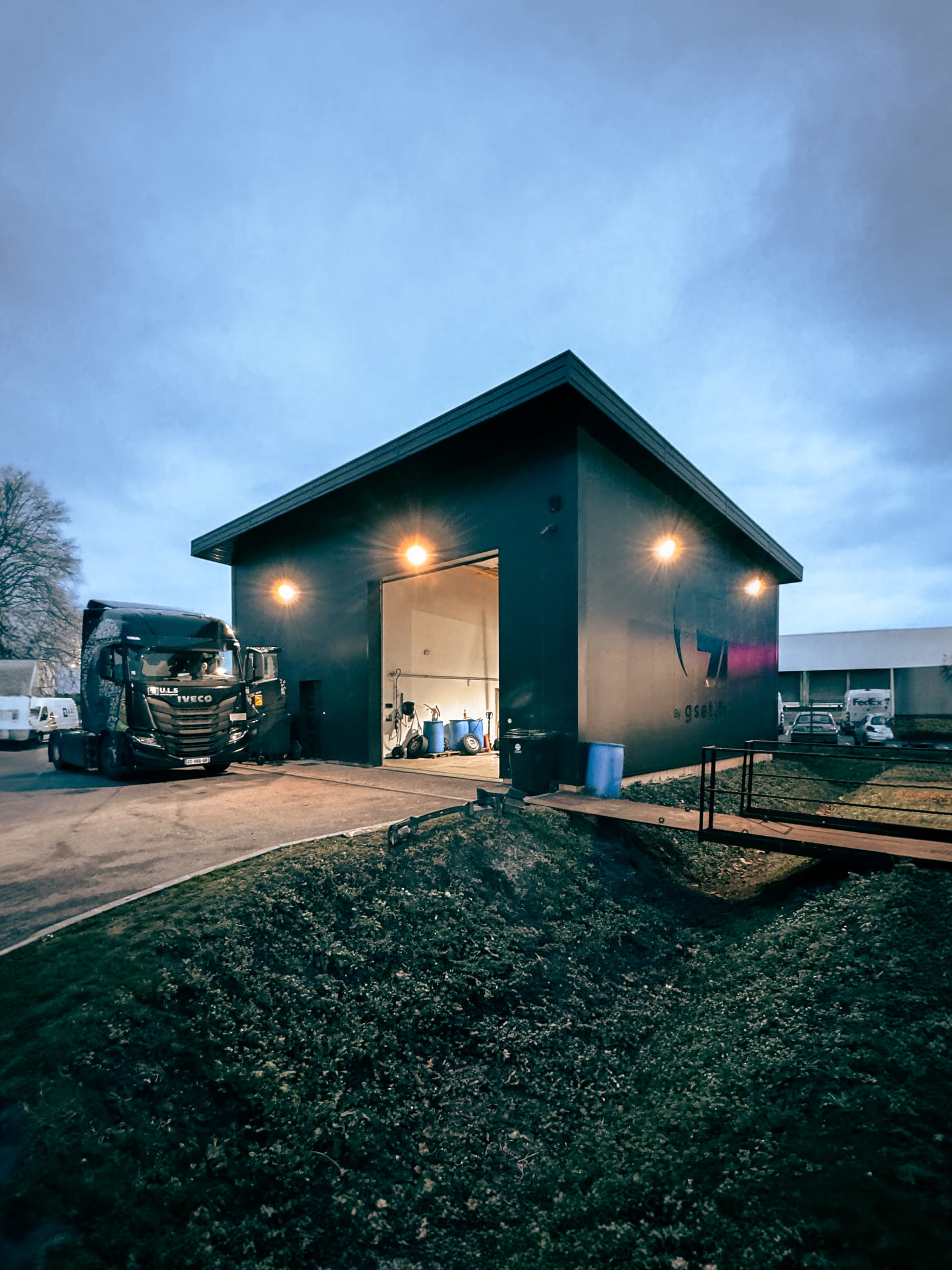 Atelier avec porte de quai ouverte, chariots et matériel de manutention en extérieur.