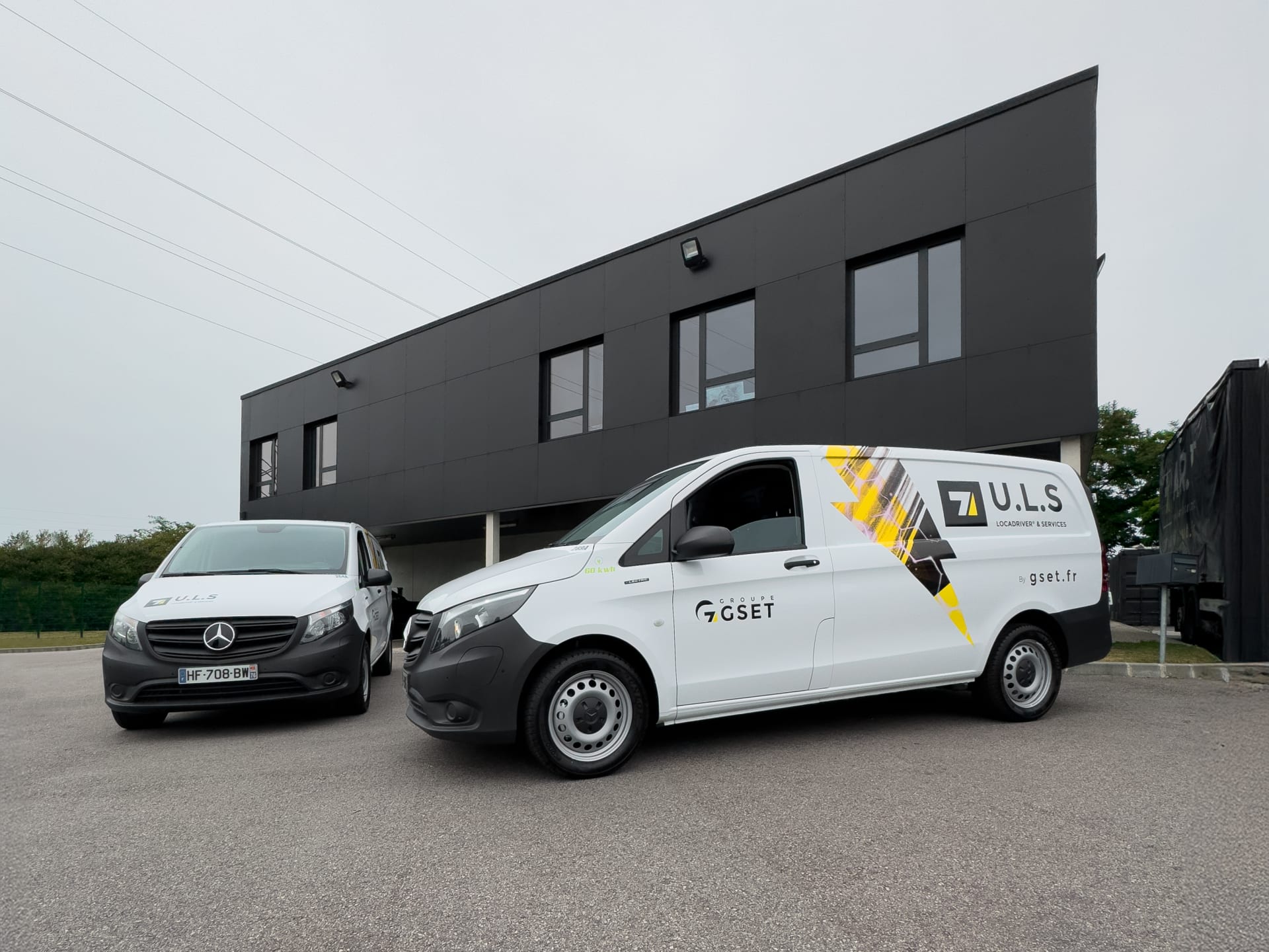 Collaborateurs du Groupe GSET réunis dans le hall d’accueil, portant des sweats noirs au logo jaune de l’entreprise, certains de face et d’autres de dos, posant devant le mur en béton brut marqué du nom Groupe GSET, ambiance conviviale et cohésion d’équipe.