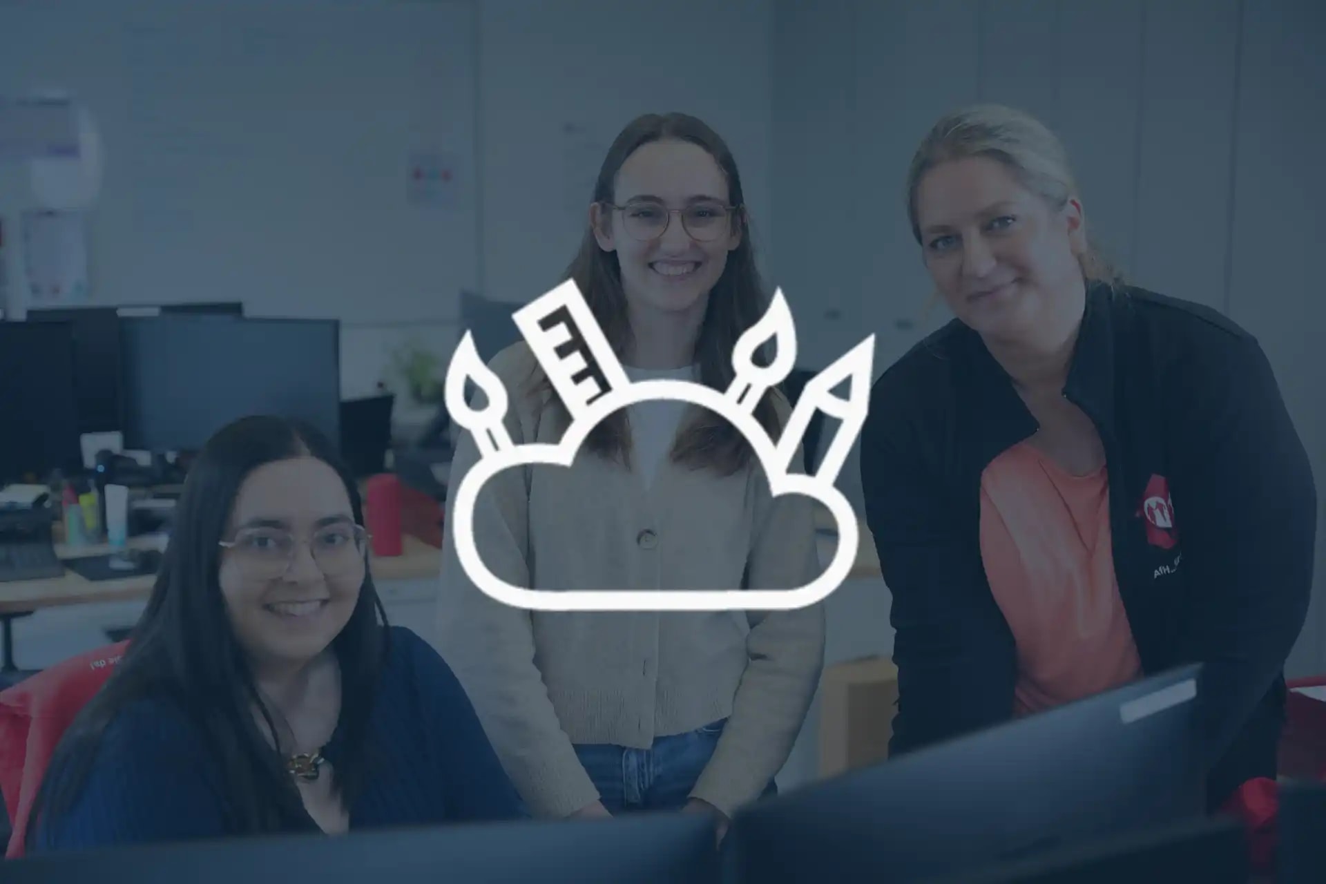 Drei Mitarbeiterinnen aus der Abteilung Marketing sitzen und stehen lächelnd am Schreibtisch