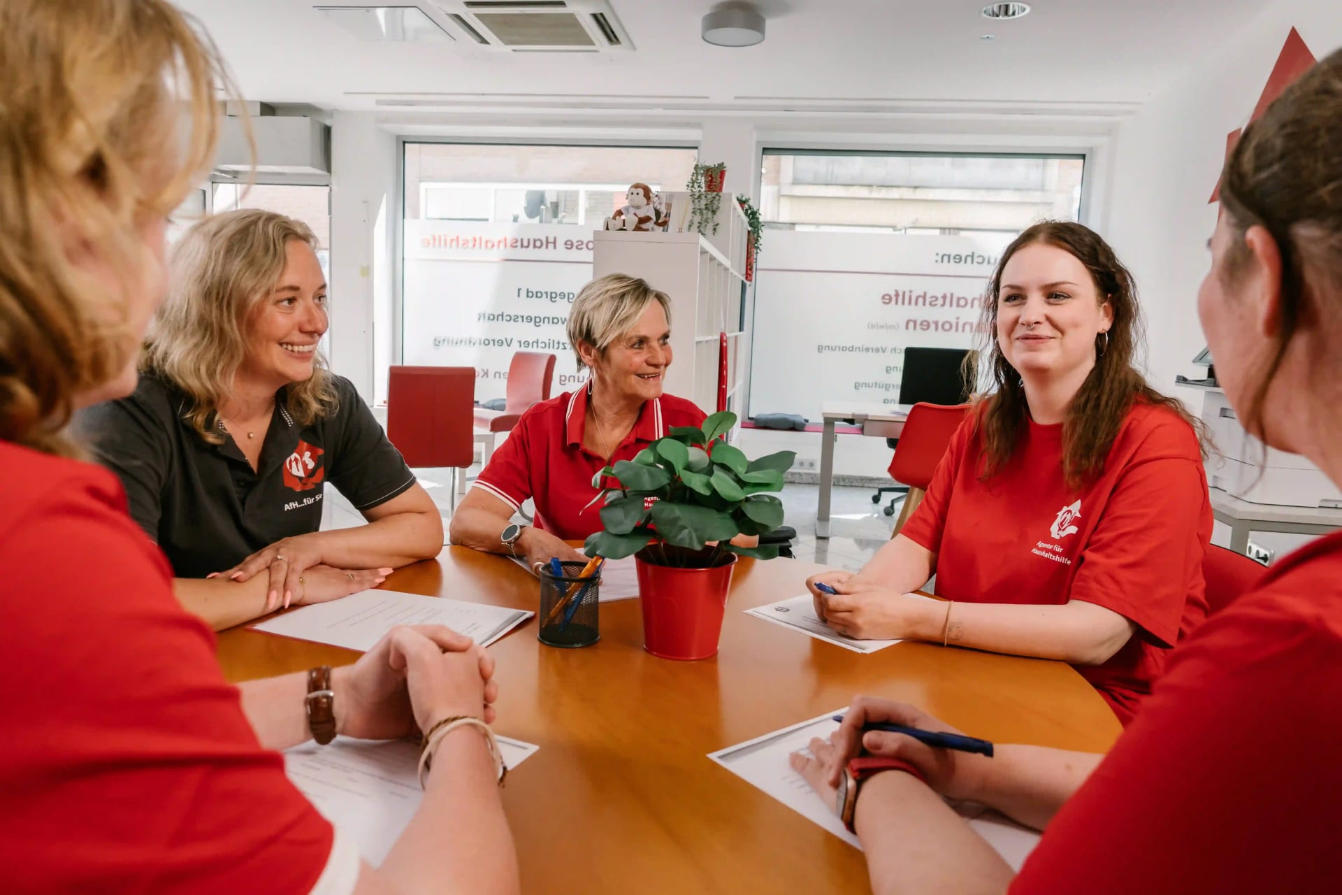Standort Teamleitung - Teamleitung und Haushaltshelfer sitzen gemeinsam fröhlich beim Teamtreffen am Tisch