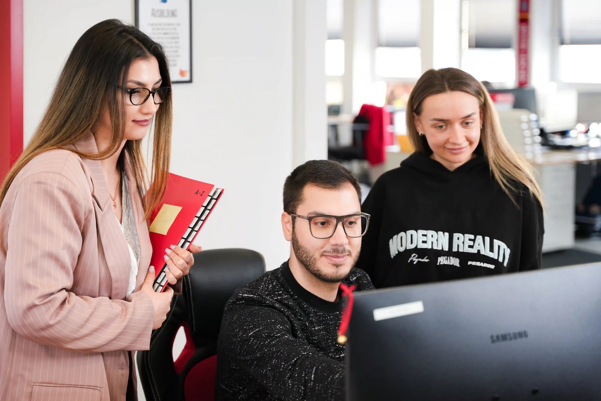 Drei Mitarbeiter der Abteilung Buchhaltung der Agentur für Haushaltshilfe schauen gemeinsam lächelnd auf einen Monitor