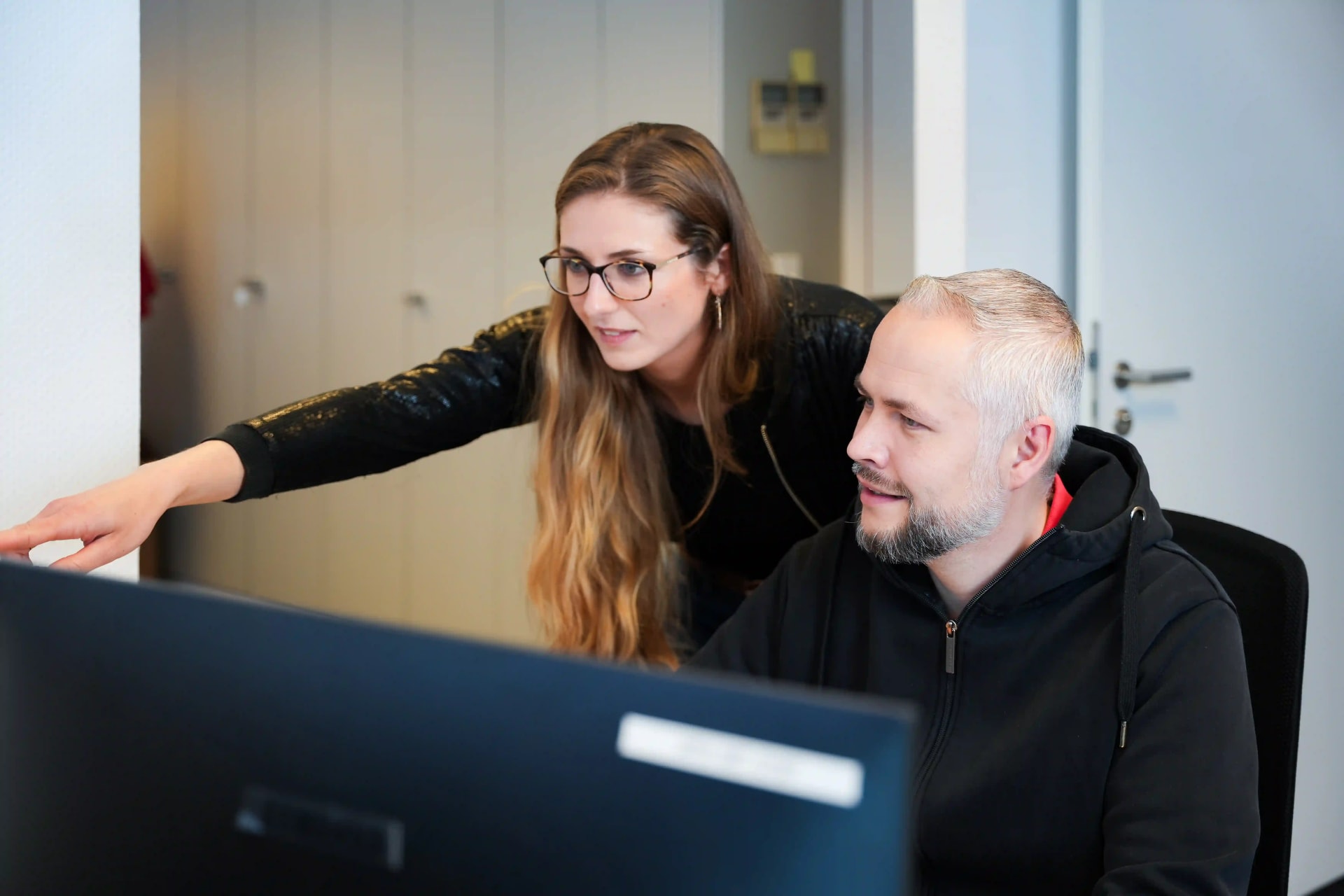 Twee medewerkers van het Recruiting team van het Agency For Domestic Help bekijken samen iets op de monitor.