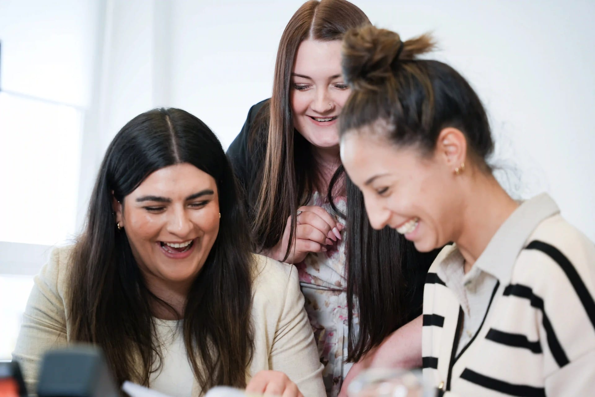 Drie medewerksters van Human Resources van het Agency For Domestic Help staan lachend bij elkaar.