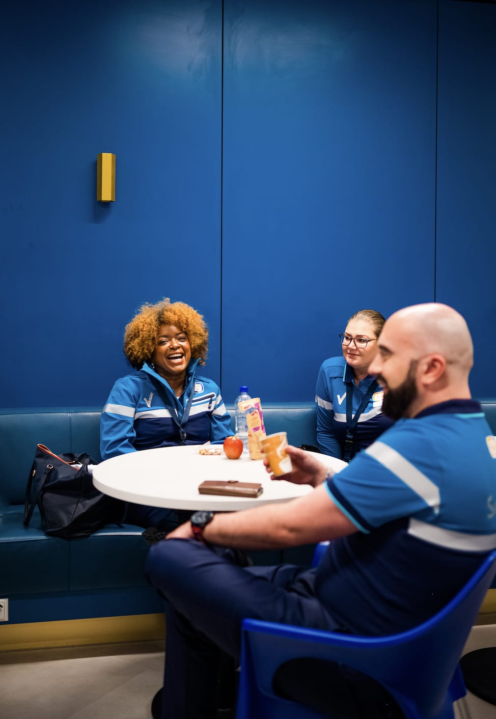 Drie beveiligingsmedewerkers in uniform genieten van een pauze en een luchtig gesprek in de blauwe personeelslounge