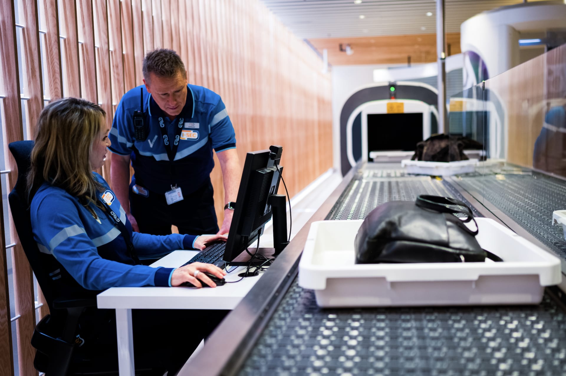 Beveiligingsmedewerkers werken samen aan een controlepunt met schermen en bagage op een luchthaven.