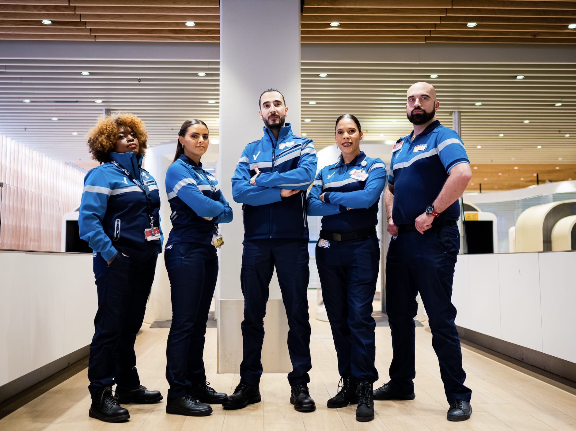 Vijf beveiligingsmedewerkers in uniform staan zelfverzekerd in een groep op Schiphol