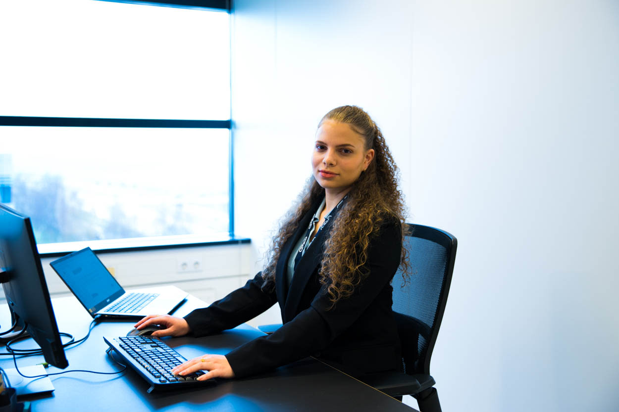 Professionele jonge vrouwelijke I-SEC medewerker werkt aan een bureau met computers in een kantoor met uitzicht op de stad