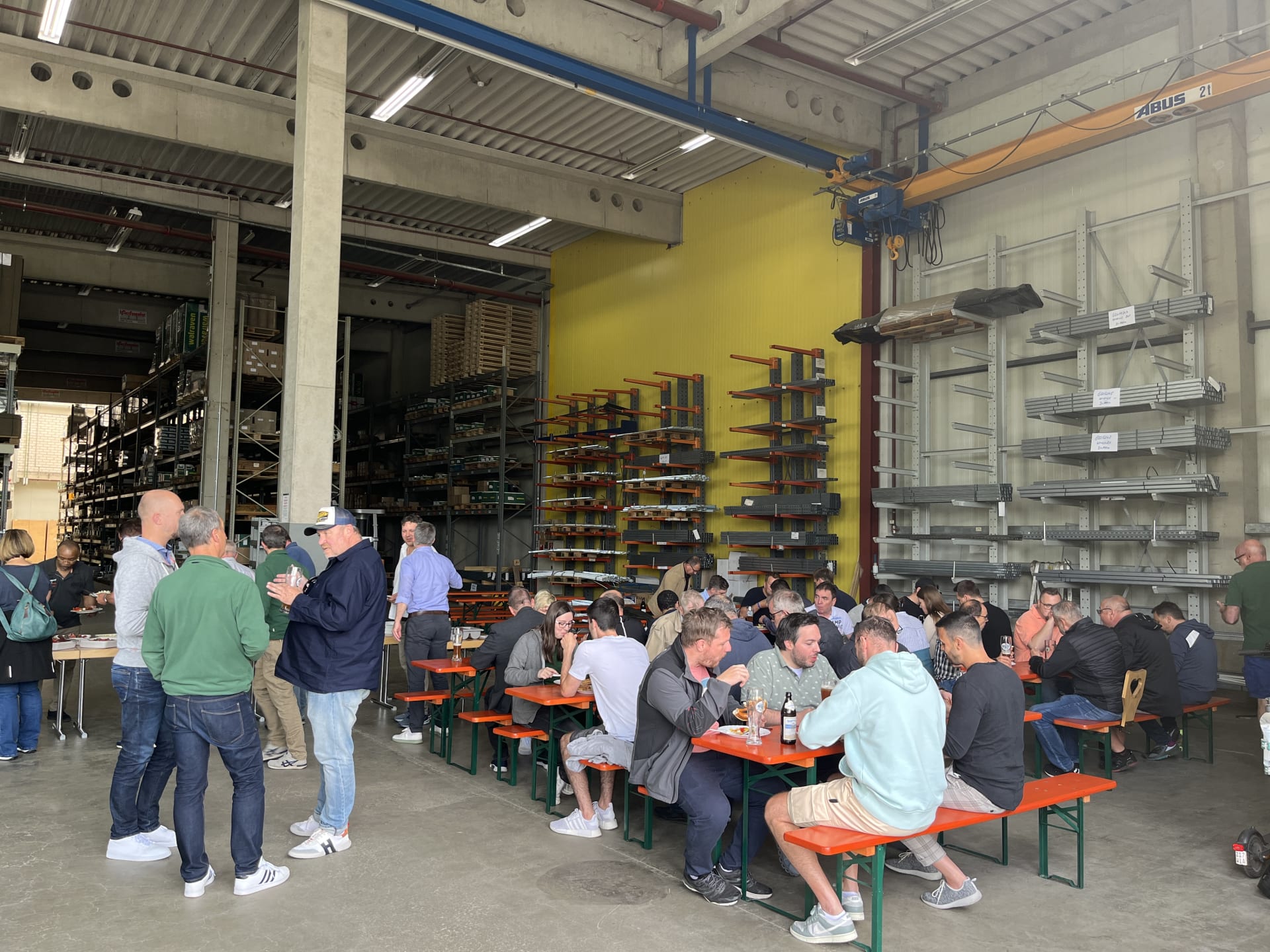 Bild aus der Lagerhalle der Walraven GmbH vom Sommerfest 2023. Dort sitzen zahlreiche Walraven-Mitarbeiter an Biertisch-Garnituren, essen und unterhalten sich.