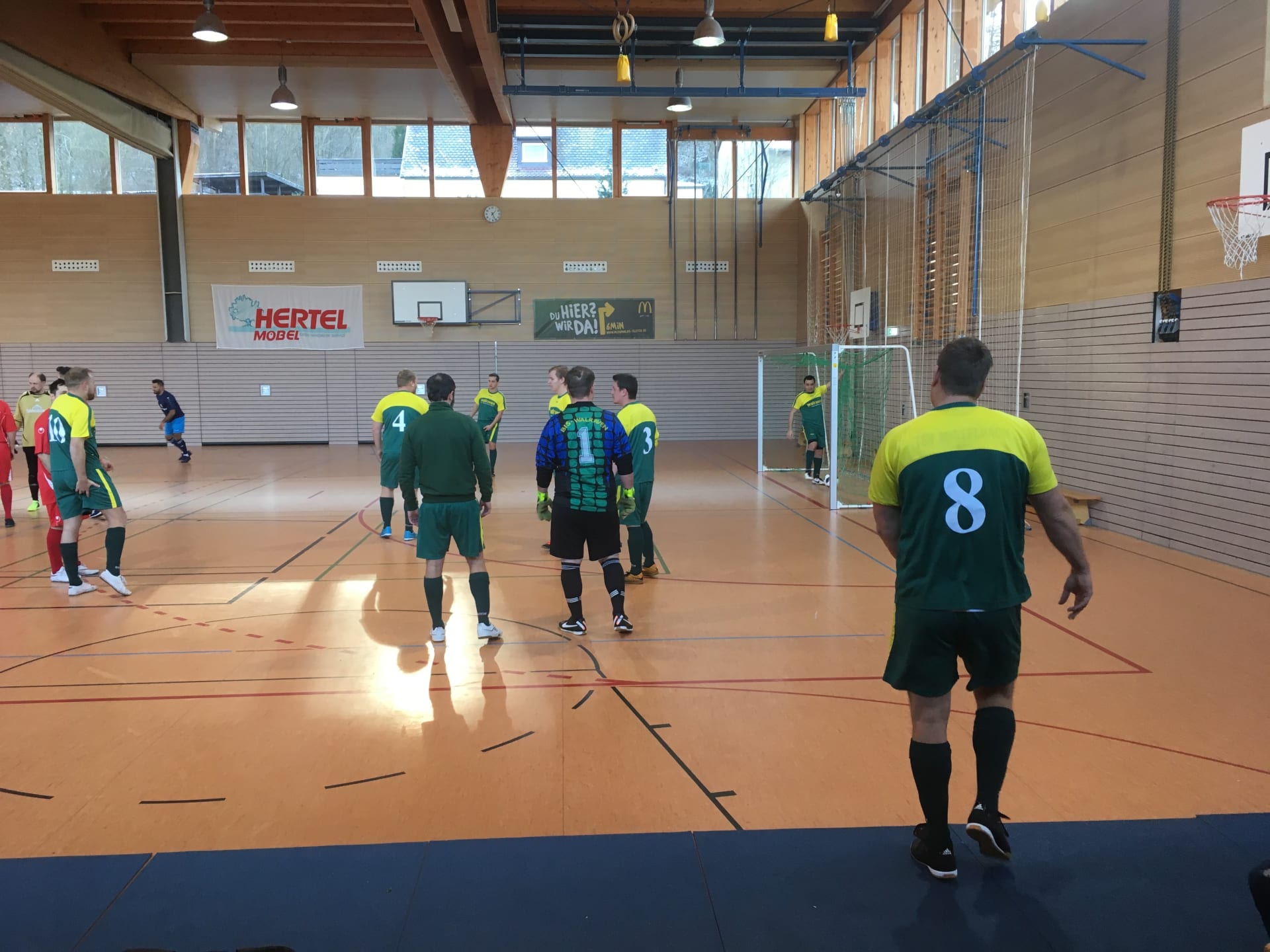 Bild aus einer Sporthalle vom Fußball Firmen-Team der Walraven GmbH. Die Spieler tragen grün-gelbe Trikots.