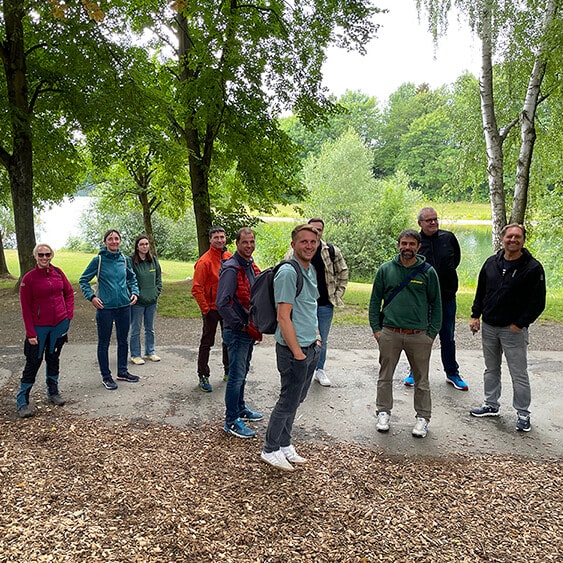 Zehn Walraven-Mitarbeiter bei einem Gruppenfoto in der Natur, im Hintergrund sind zahlreiche Bäume zu sehen, einige Mitarbeiter tragen einen Wander-Rucksack. Hier ist also eine gemeinsame Wanderung der Walraven-Mitarbeiter abgebildet.