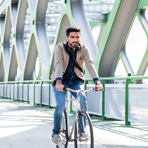 Ein Mann mittleren Alters fährt Fahrrad auf einer Brücke mit grünen Pfeilern, er schaut entschlossen Richtung Kamera. Das Bild steht symbolisch für den Walraven Mitarbeiterbenefit "Dienstrad-Leasing"