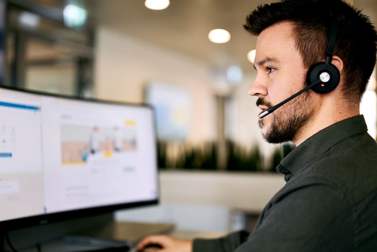 Ein Mitarbeiter mit Headset auf der konzentriert vor einem Bildschirm sitzt.