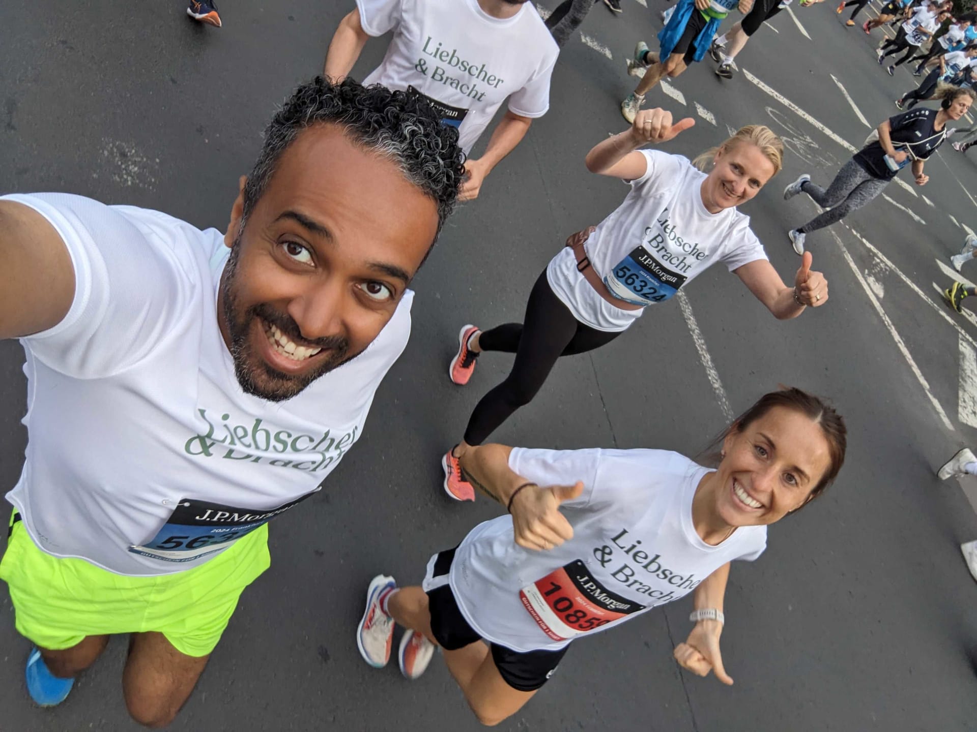 Eine Gruppe von Menschen läuft gemeinsam bei dem JP Morgan Lauf in Frankfurt am Main mit und zeigt Teamgeist und Ausdauer. Sie tragen weiße T-Shirts auf denen in grün das Liebscher & Bracht Logo zu sehen ist. Sie schauen glücklich in die Kamera.