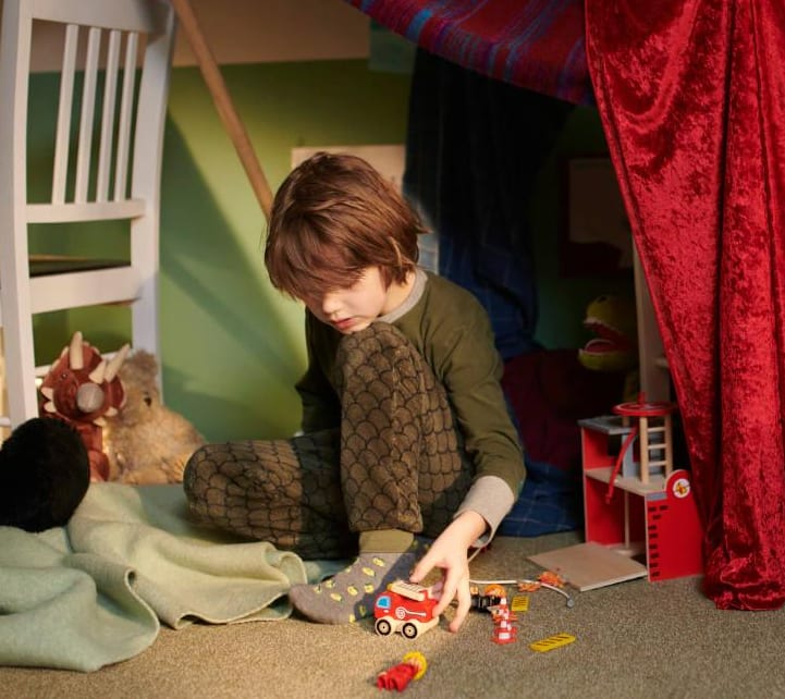 Een jongetje zit op de grond en speelt met zijn speelgoed in zijn kinderslaapkamer