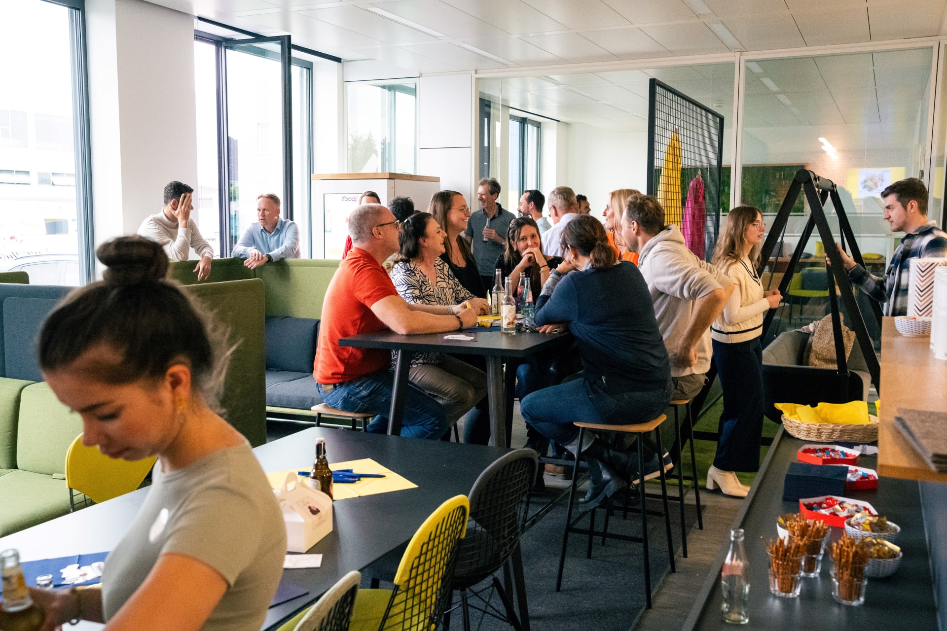 Eine Gruppe Mitarbeitender sitzt an einem Hocktisch und unterhält sich bei einem After-Work Event.