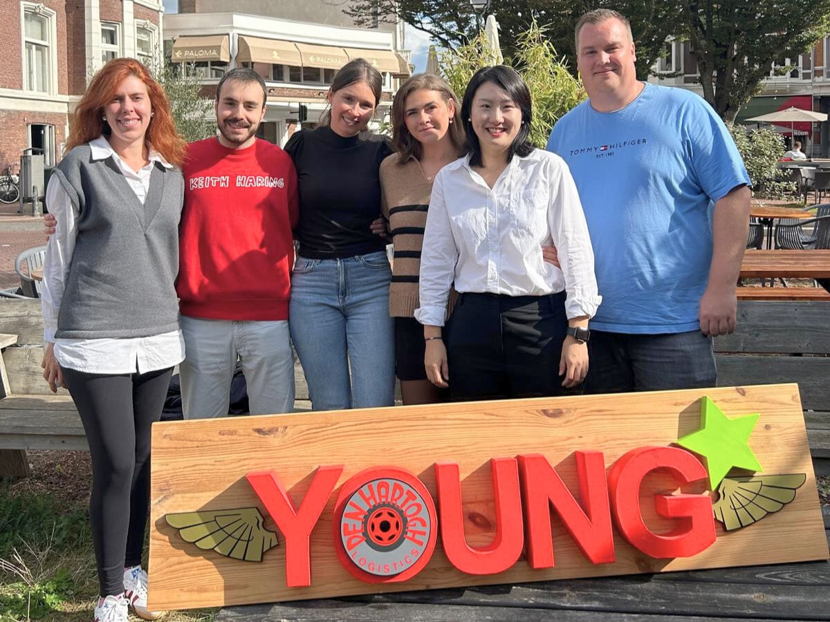 A group of young people outside posing in front of a sign reading 'YOUNG'