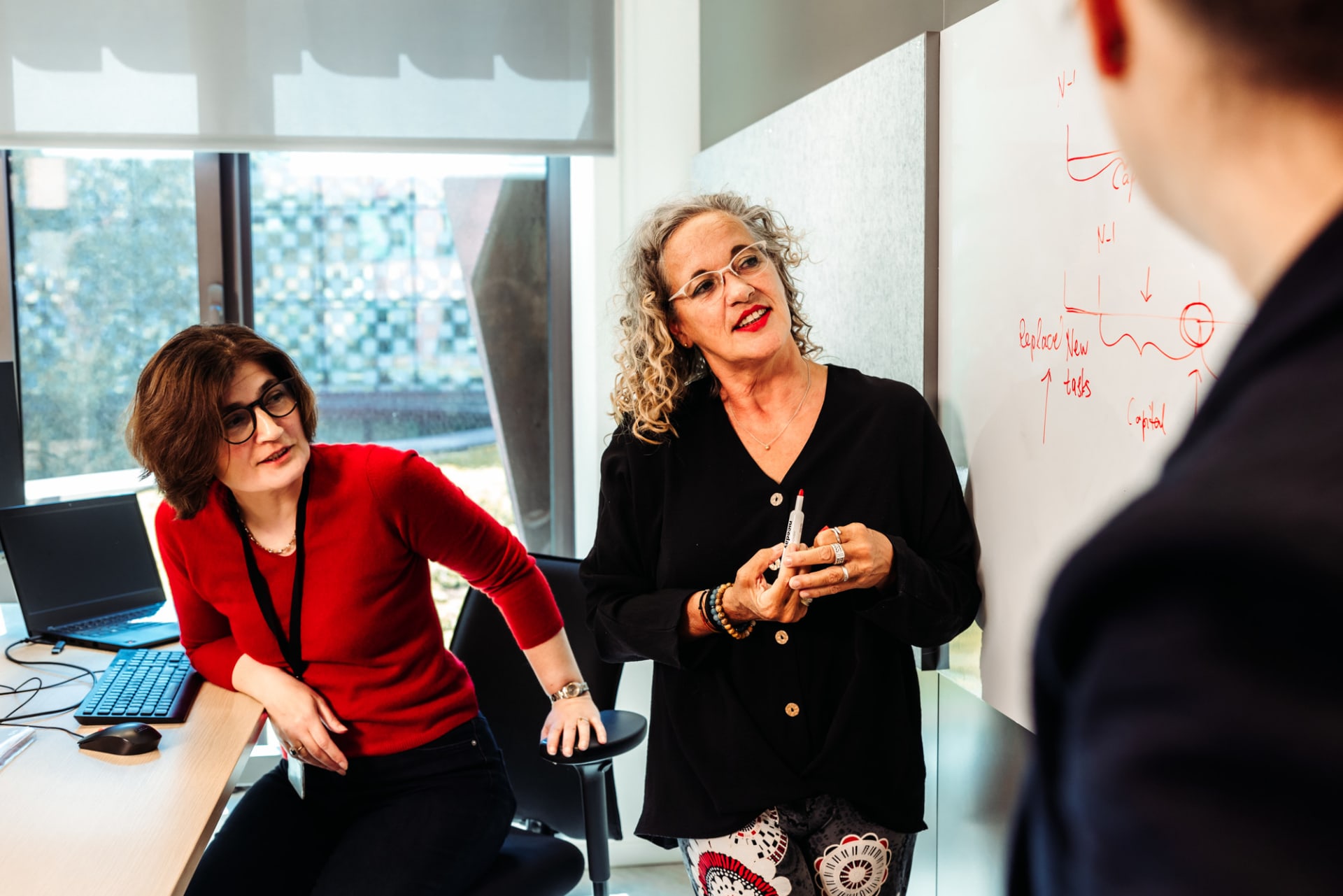 Twee collega's staan bij een whiteboard en overleggen