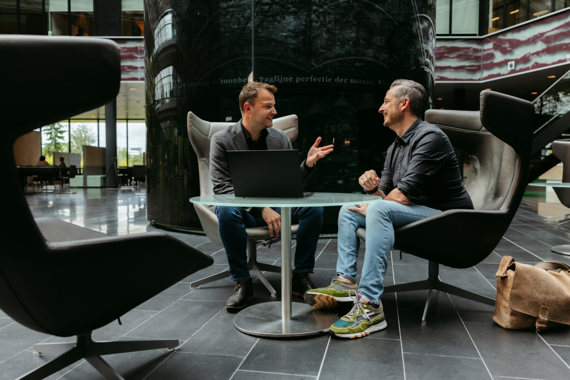 Twee collega's in overleg op relaxte fauteuils in een atrium in Heerlen