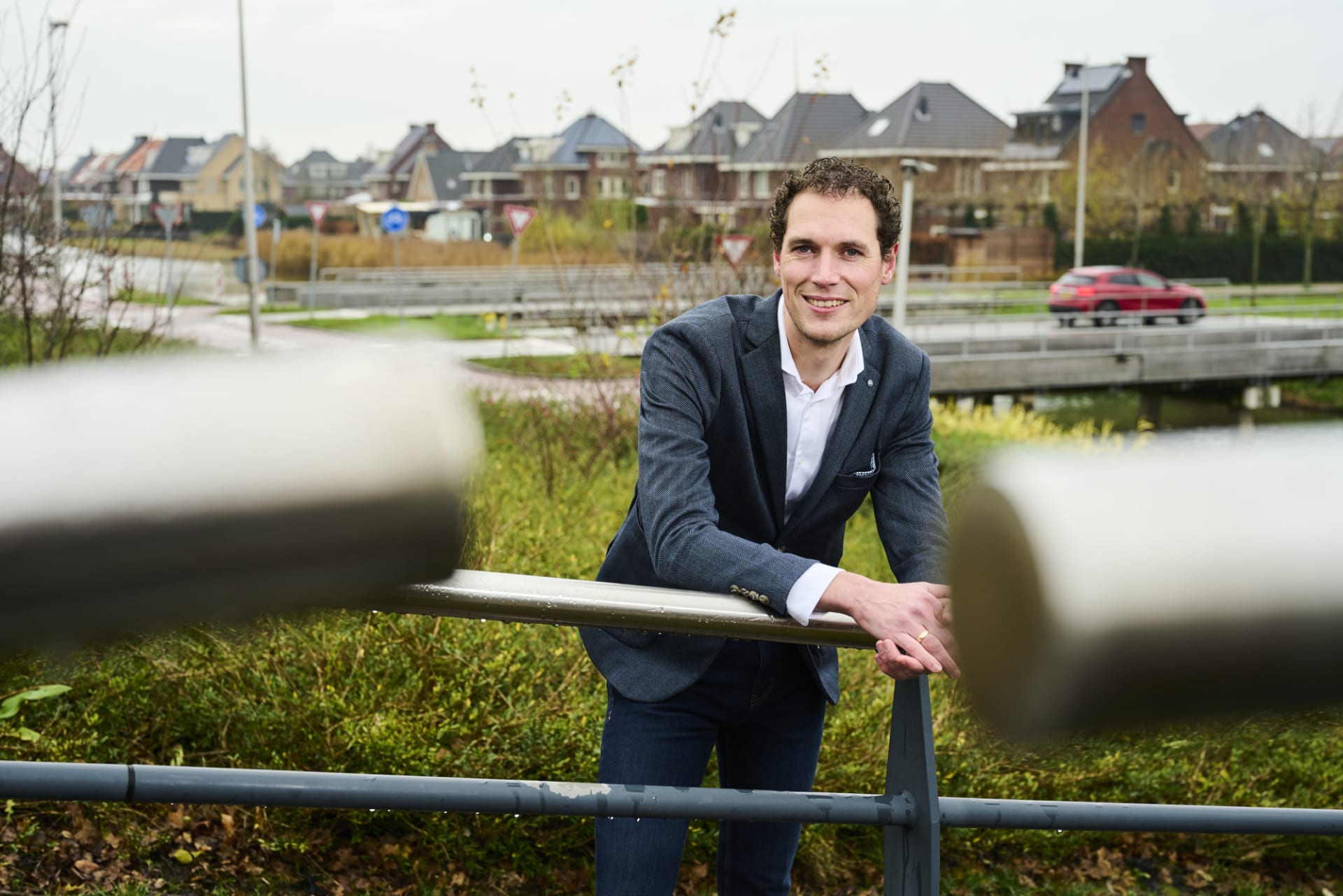 Walter lacht in de camera op een brug voor een woonwijk