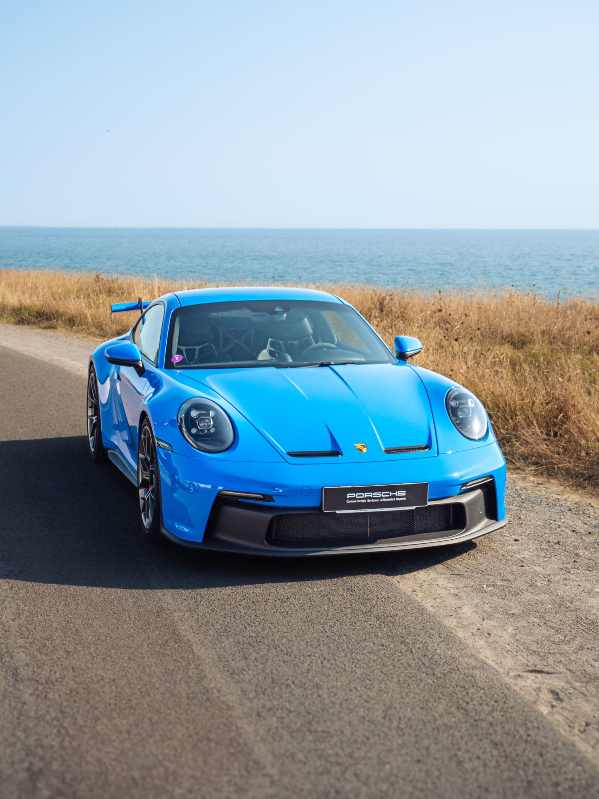 Porsche bleue sur route côtière avec les Centres Porsche RCM