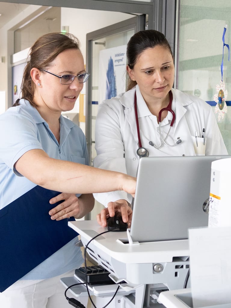 Pflegekraft und Ärztin beraten sich vor Laptop am Gang der Albert Schweitzer Klinik