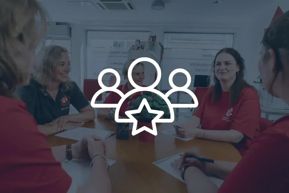 Standort Teamleitung - Teamleitung und Haushaltshelfer sitzen gemeinsam fröhlich beim Teamtreffen am Tisch