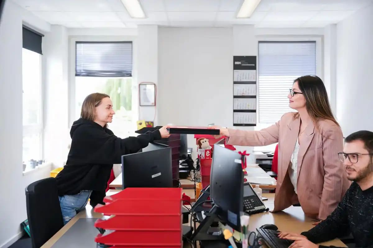 De medewerkers van het Boekhouding team op kantoor geven elkaar een dossier door.