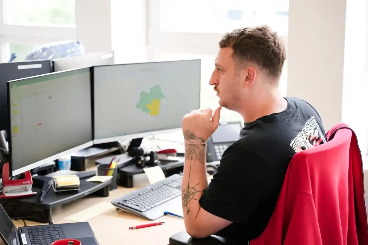 Een medewerker van de afdeling Buitendienst Coordination van AGFH Huishoudelijke Hulp zit aan zijn bureau en kijkt naar twee beeldschermen.