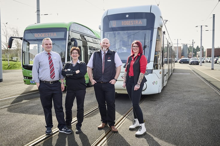 Vier Bus- und Straßenbahnfahrer*innen stehen vor einem Bus und einer Straßenbahn.