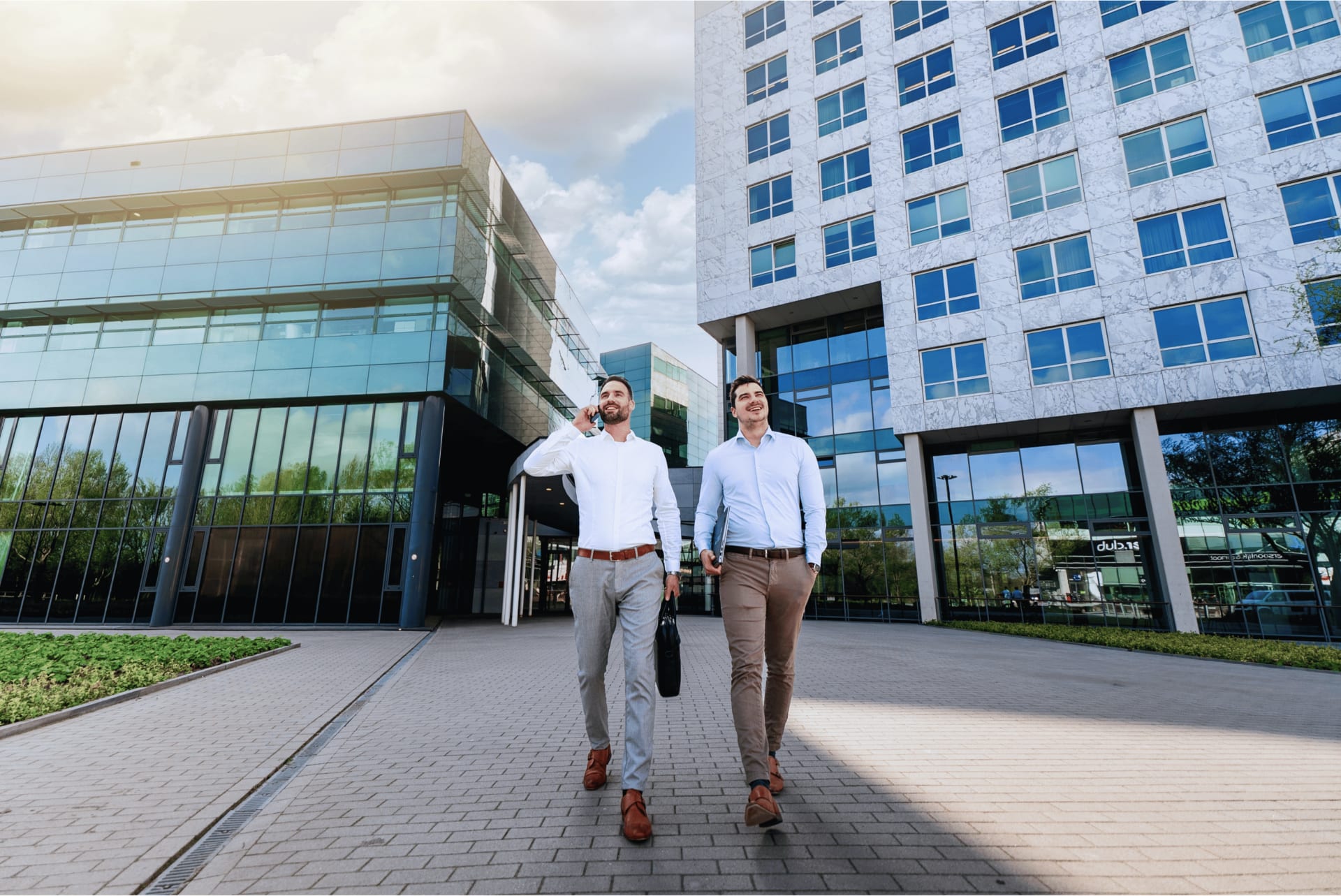 Twee lachende collega's lopen het pand uit, één van hen belt