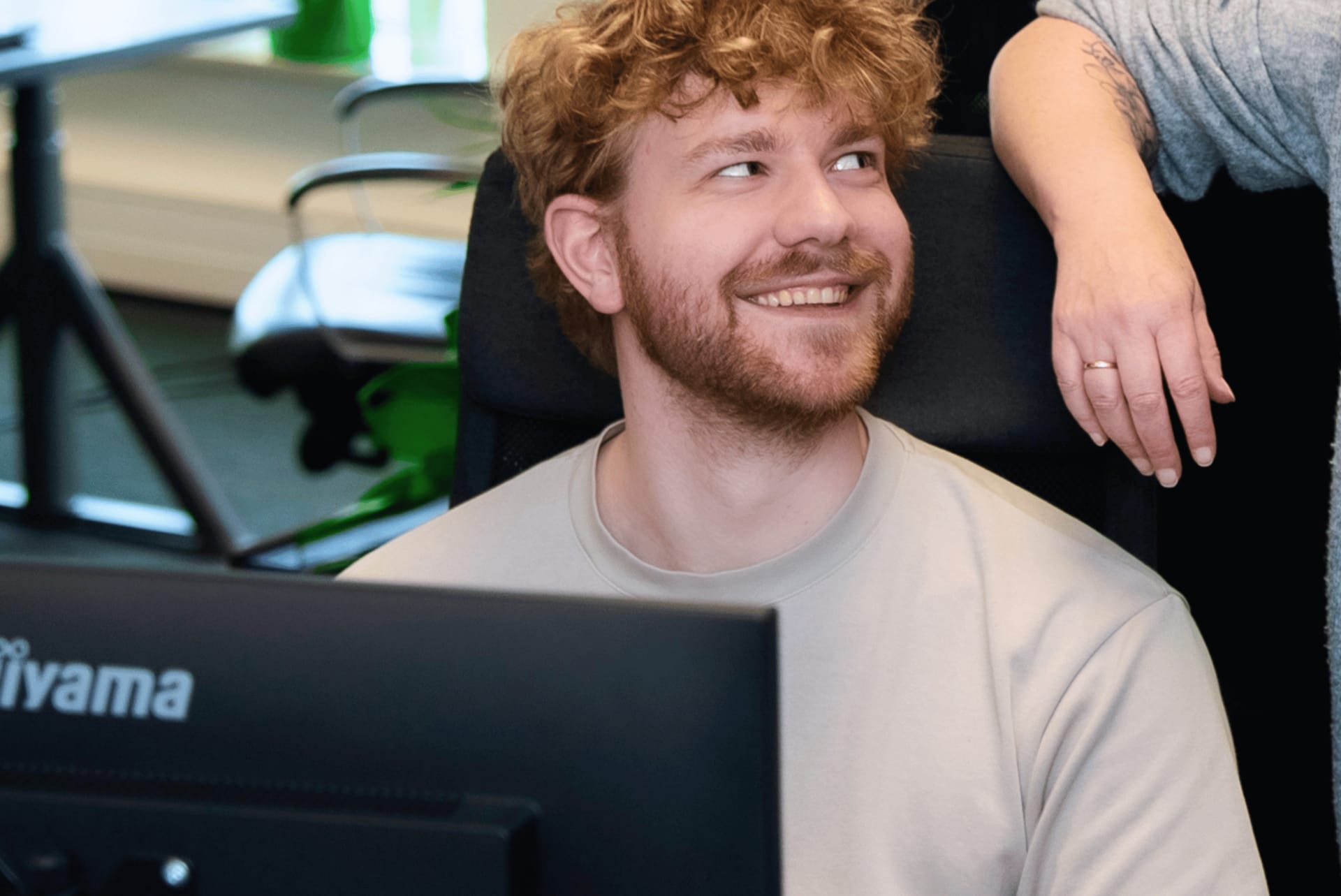 Een lachende collega zit achter een laptop en kijkt naar de collega naast hem