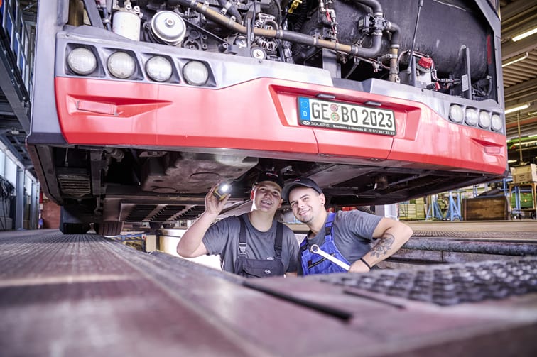 Zwei junge Männer befinden sich in einer Arbeitsgrube unter einem BOGESTRA-Bus und schauen sich den Bus von unten an.