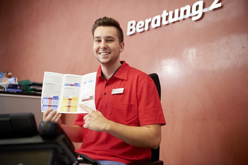 Ein junger Mann in Dienstkleidung hält ein Prospekt in der Hand und zeigt mit dem Finger darauf.