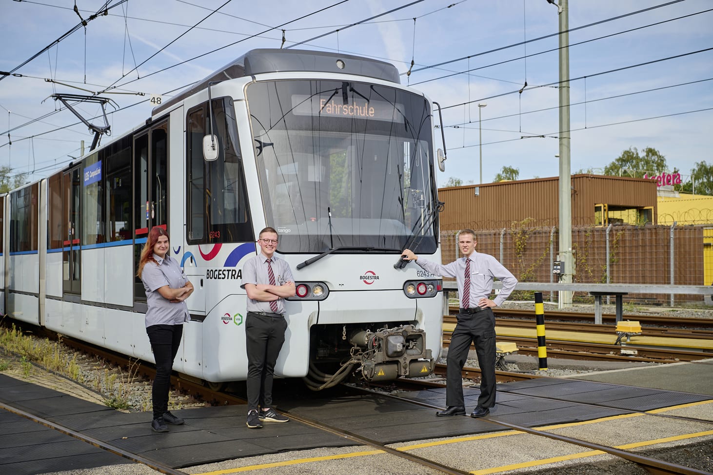 Drei junge Mitarbeiter stehen vor einer Fahrschul-Straßenbahn.