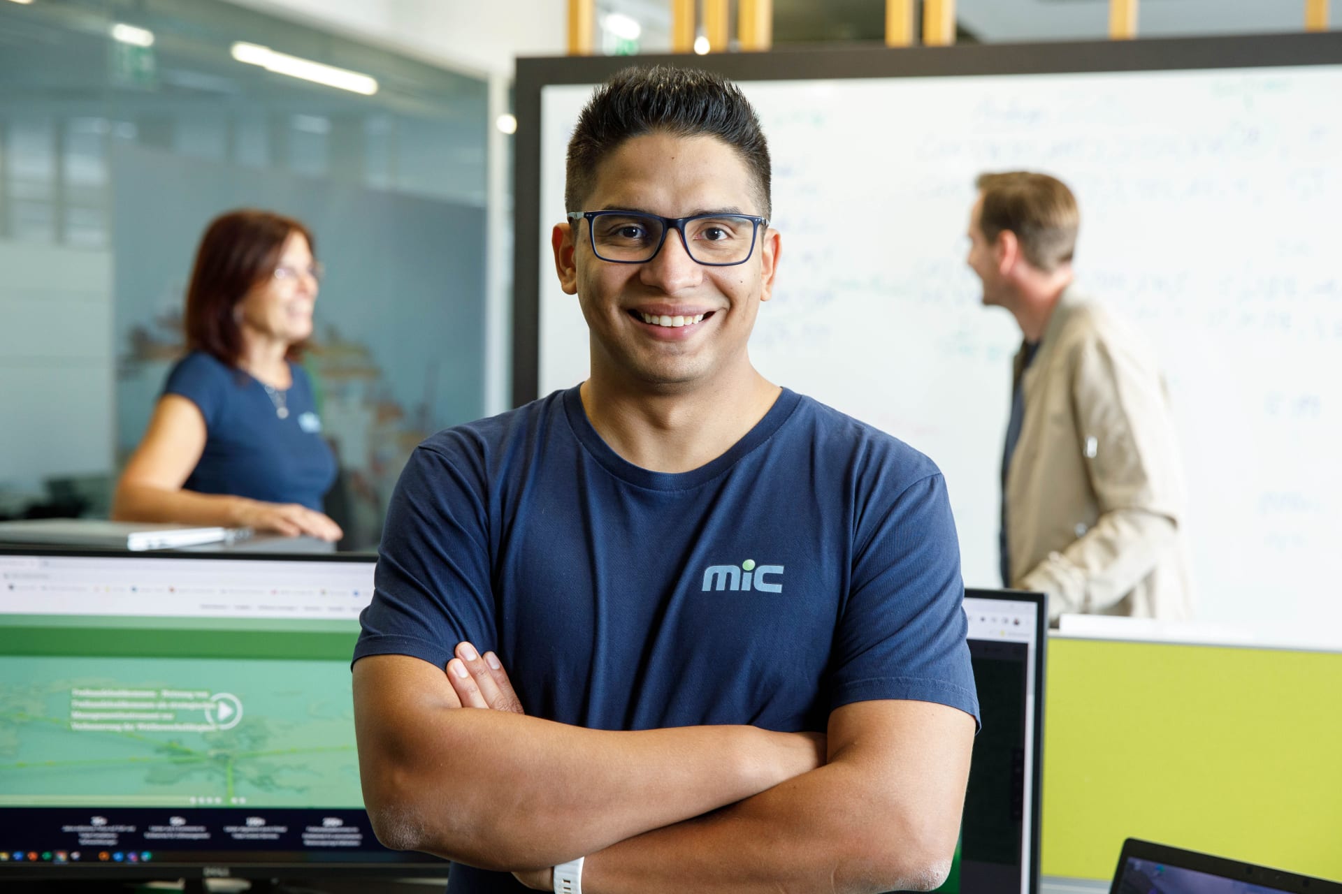 Smiling MIC employee in a branded T-shirt with colleagues in the office
