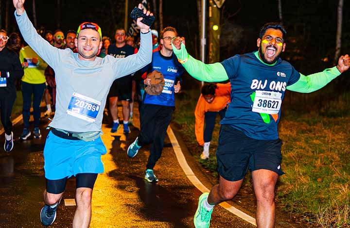 Deelnemers aan de Leiden Marathon, waaronder een hardloper in een blauw Zorg en Zekerheid-shirt die met gespreide armen over het parcours rent.